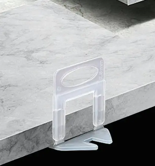 Clear tile leveling clip holding the edges of two marble-effect tiles flush